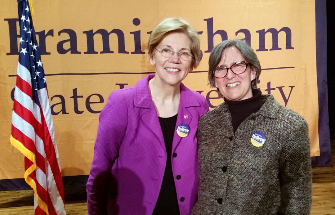 Elizabeth Warren and Gwendolyn Holbrow with an American flag and campaign buttons on the stage at Framingham State University.
