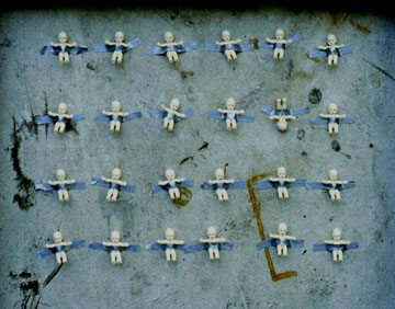 24 tiny plastic babies are taped to a stained formica wall with duct tape.